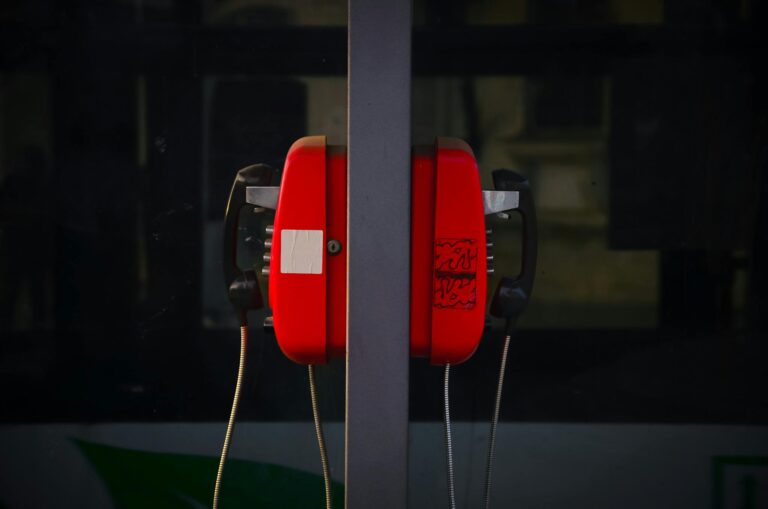 A retro red telephone booth with a reflective glass surface in an urban environment.