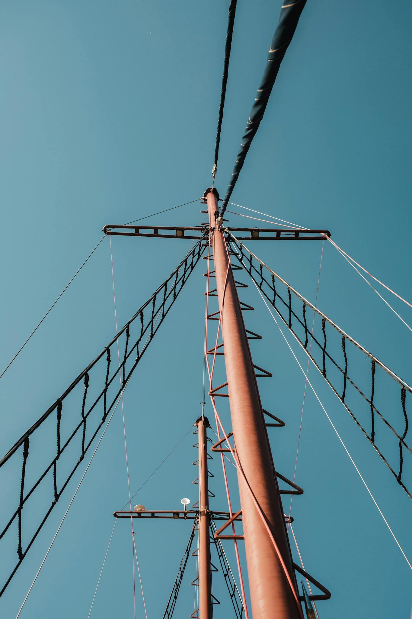 A vertical shot of a tall metal structure with cables against a clear blue sky.