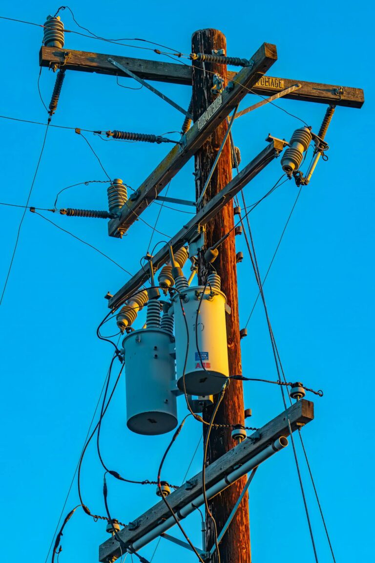 Low-angle view of utility pole with power lines against a clear blue sky, highlighting industrial design.